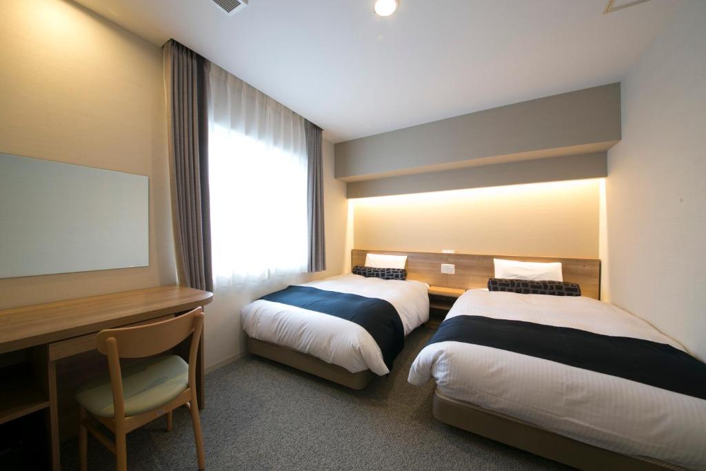 a hotel room with two beds and a desk and a television at Just Inn Premium Nagoya Station in Nagoya