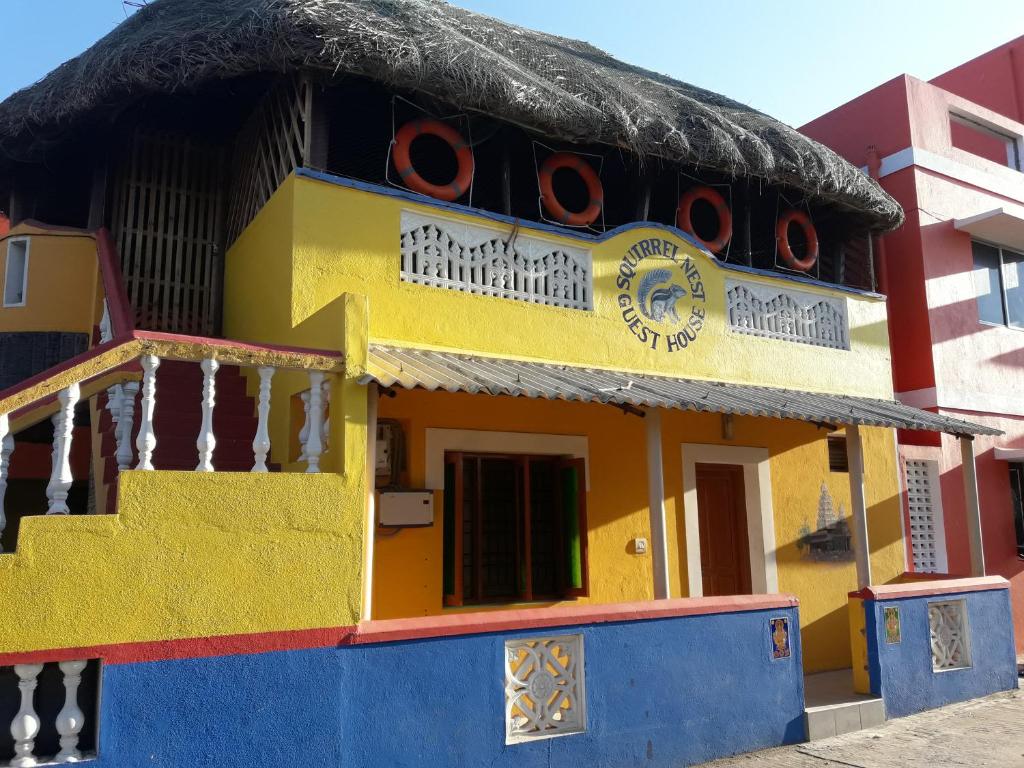 een geel en blauw gebouw met een rieten dak bij Squirrel Nest Guest House in Mahabalipuram