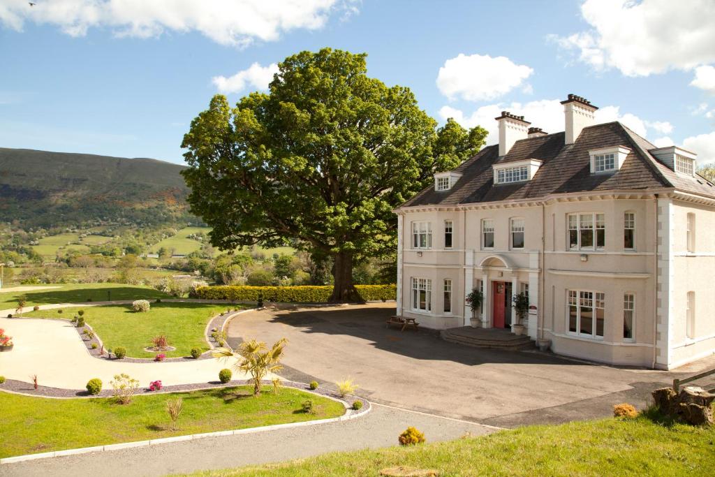 a large white house on a hill with a tree at Kilmore Country House in Glenariff