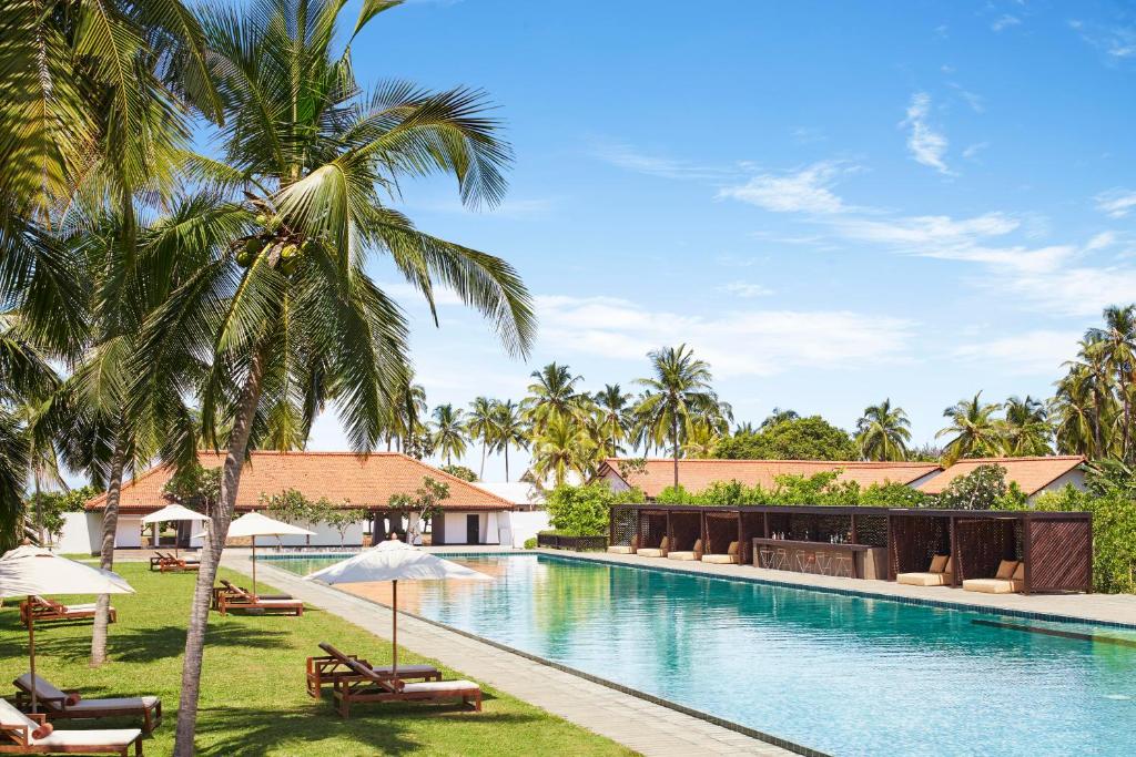 uma piscina no resort com palmeiras e guarda-sóis em Jetwing Lagoon em Negombo