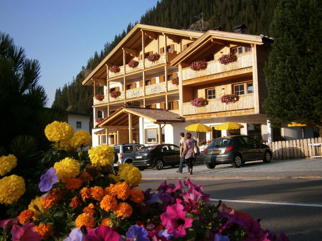 a building with cars parked in front of it with flowers at Monti Pallidi B&B Apartments in Corvara in Badia
