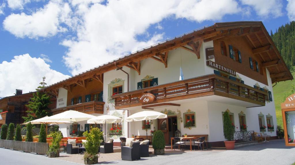 ein Gebäude mit einem Balkon, Tischen und Sonnenschirmen in der Unterkunft Hotel Hartenfels in Lech am Arlberg