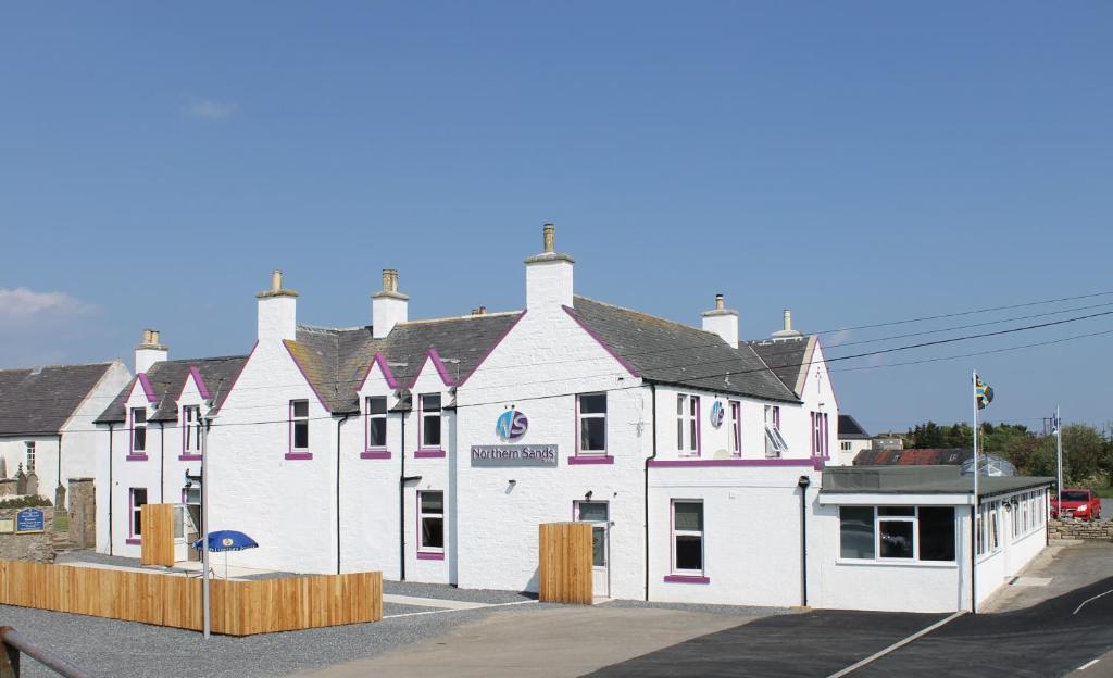 a large white building with pink accents on a street at Northern Sands Hotel in Dunnet