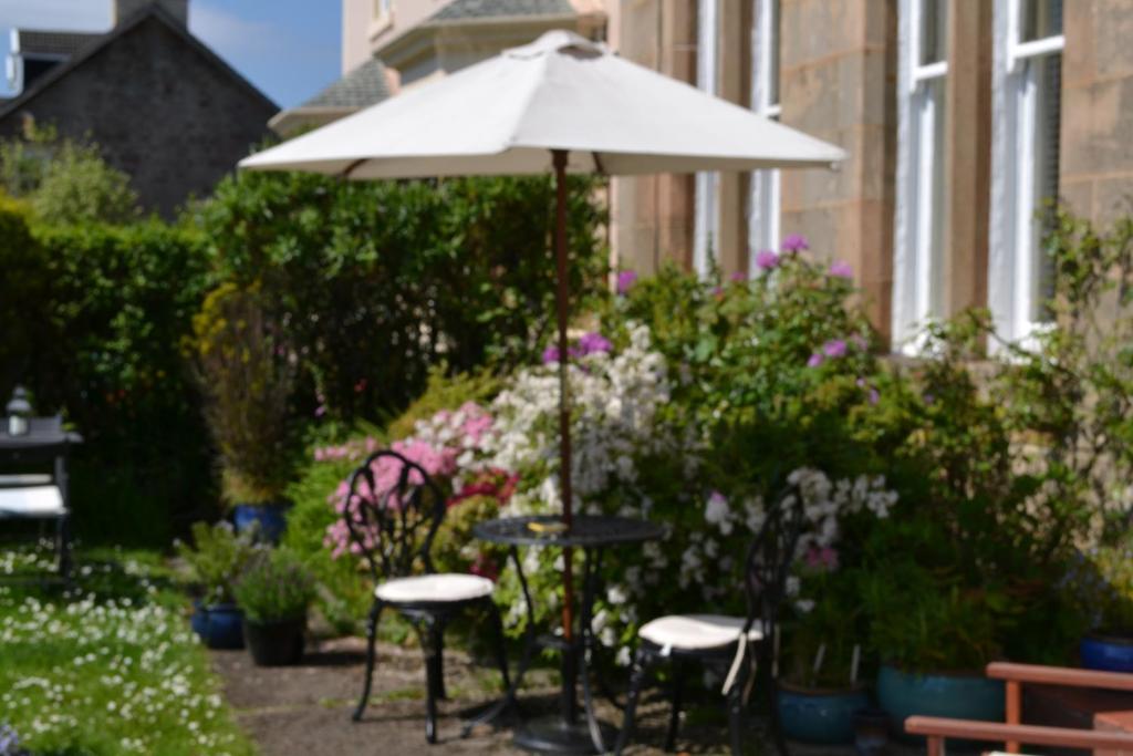 an umbrella and tables and chairs in a garden at Maybank Guest House in Helensburgh