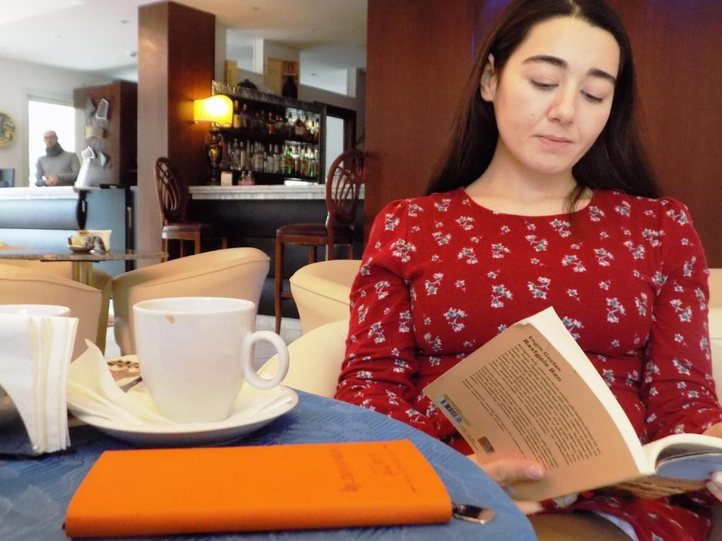 a woman sitting at a table reading a book at Hotel Residence Villa Del Mare in Rimini