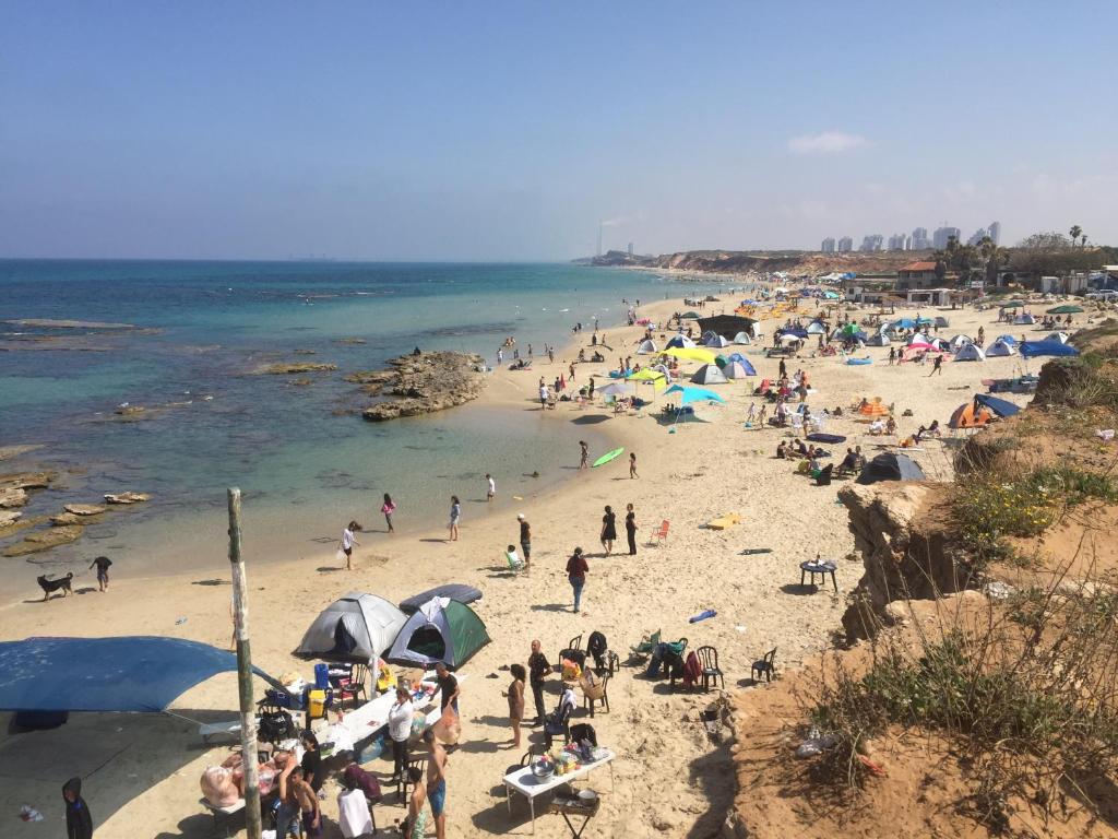 um grupo de pessoas em uma praia com guarda-sóis em Caravans through the nature em Mikhmoret