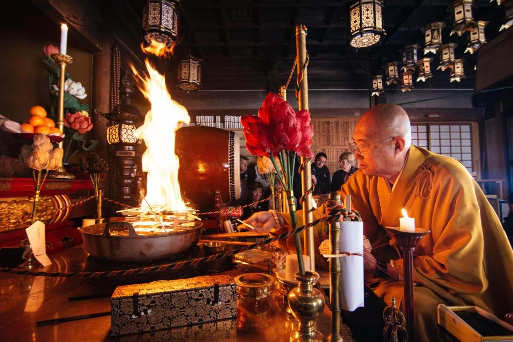 um monge sentado numa mesa numa sala com uma lareira em 高野山 宿坊 熊谷寺 -Koyasan Shukubo Kumagaiji- em Koyasan