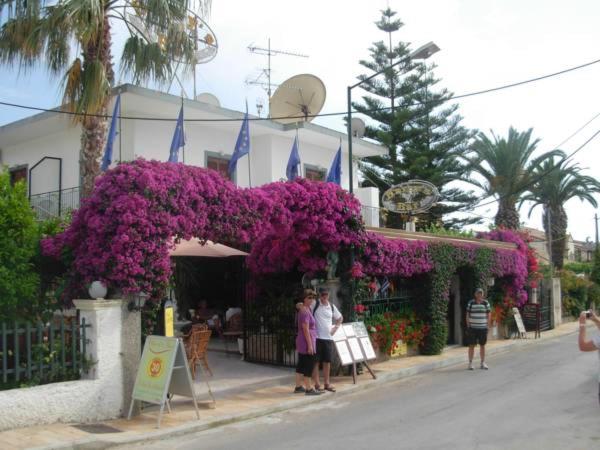 eine Gruppe von Menschen, die vor einem Gebäude mit lila Blumen stehen in der Unterkunft Harry's Bar & Apartments 1 in Acharavi