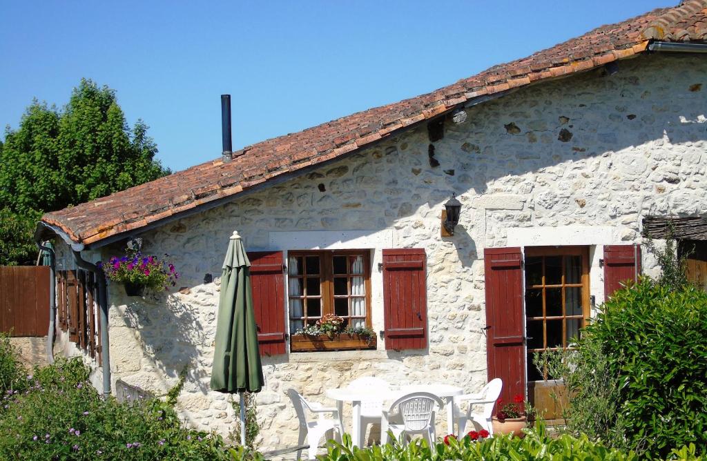 Casa de piedra con sombrilla, mesa y sillas en Gîte Chez Marot, en Varaignes