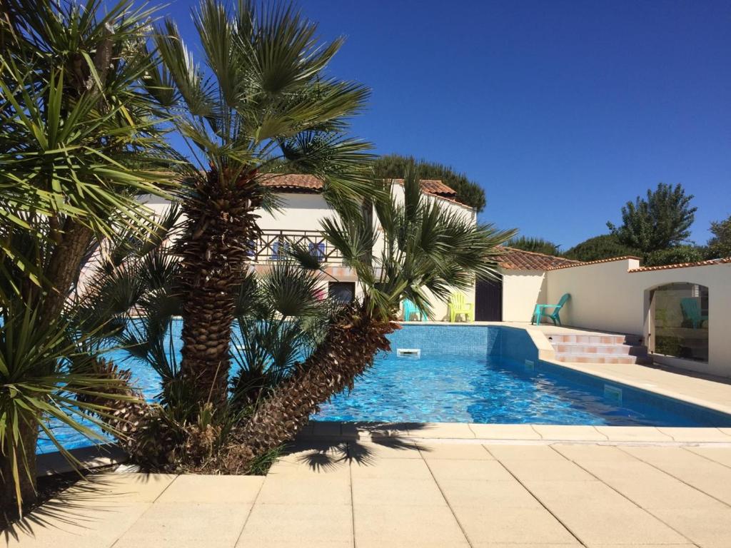 a swimming pool with palm trees in front of a house at Camping Barataud in Saint-Denis-dʼOléron