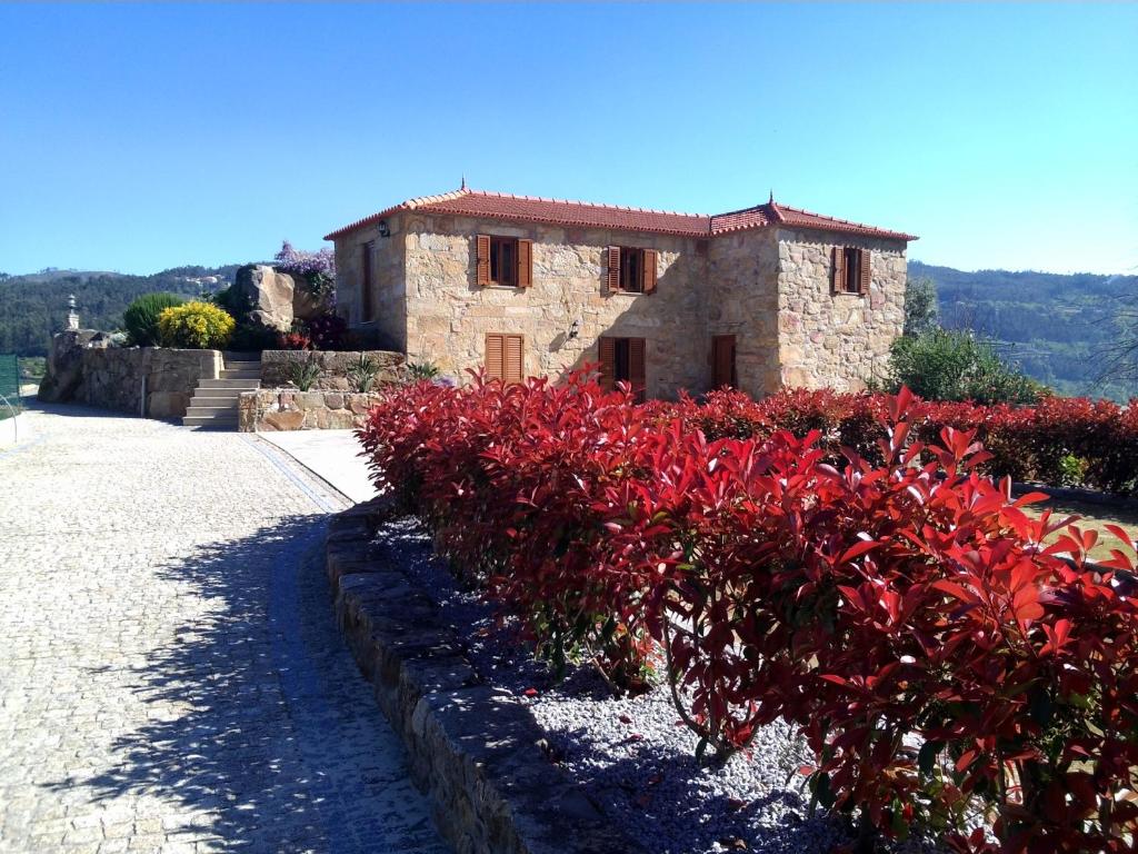 a stone house with red bushes in front of it at Casa do Alto in Magrelos