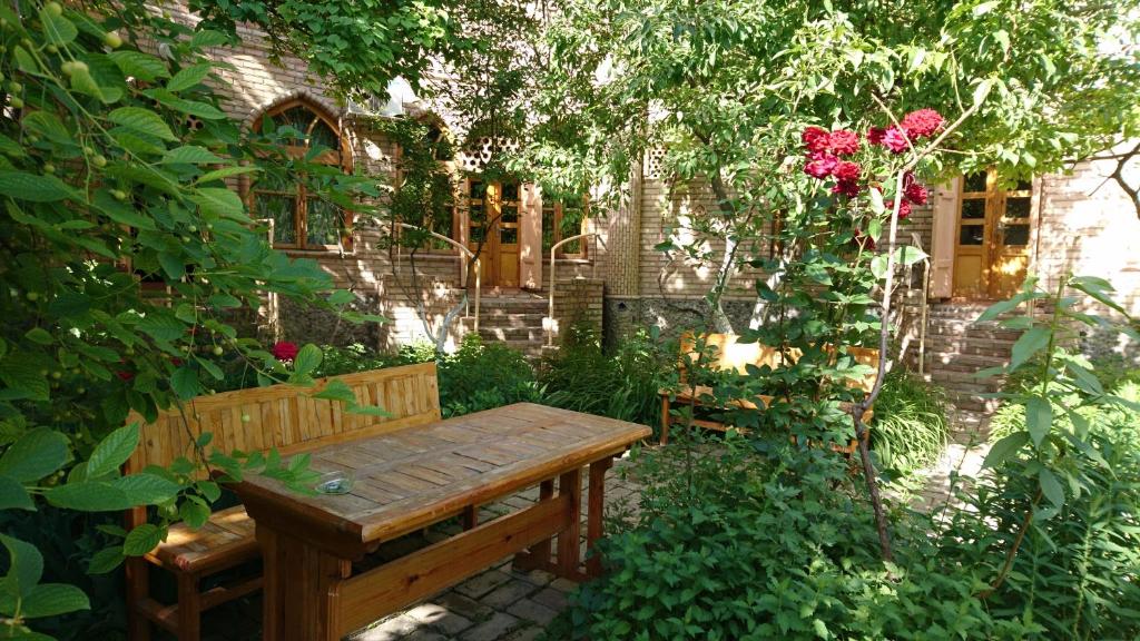 eine Holzbank in einem Garten mit Rosen in der Unterkunft ANTICA Family Guest House in Samarkand