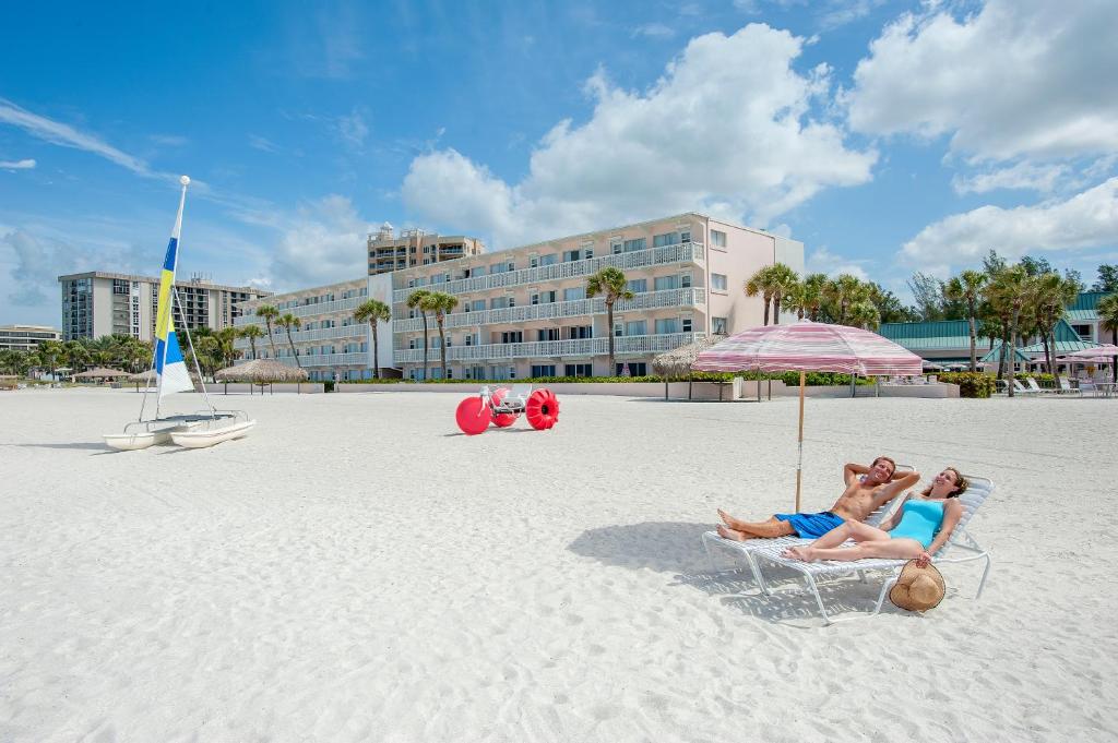 two people sitting in a chair under an umbrella on the beach at Sandcastle Resort at Lido Beach in Sarasota