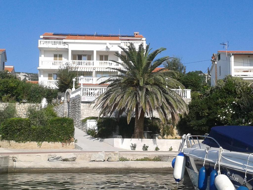 a building with a palm tree and a boat in the water at Apartments and Rooms Vinko in Barbat na Rabu