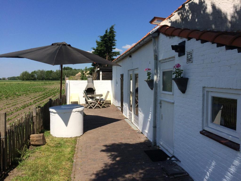 a white building with an umbrella next to a field at Farmhouse near beach in Kloosterzande