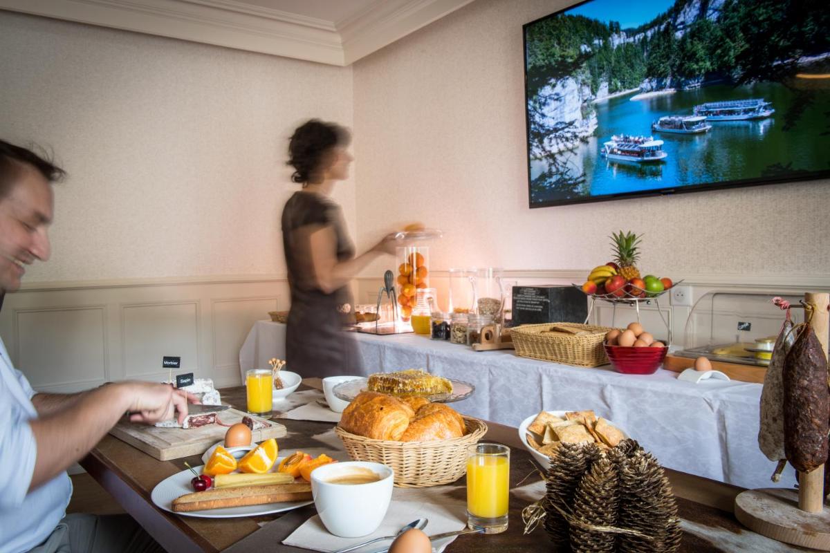un homme et une femme debout devant une table avec de la nourriture dans l'établissement Logis Hotel Restaurant Le France, à Villers-le-Lac