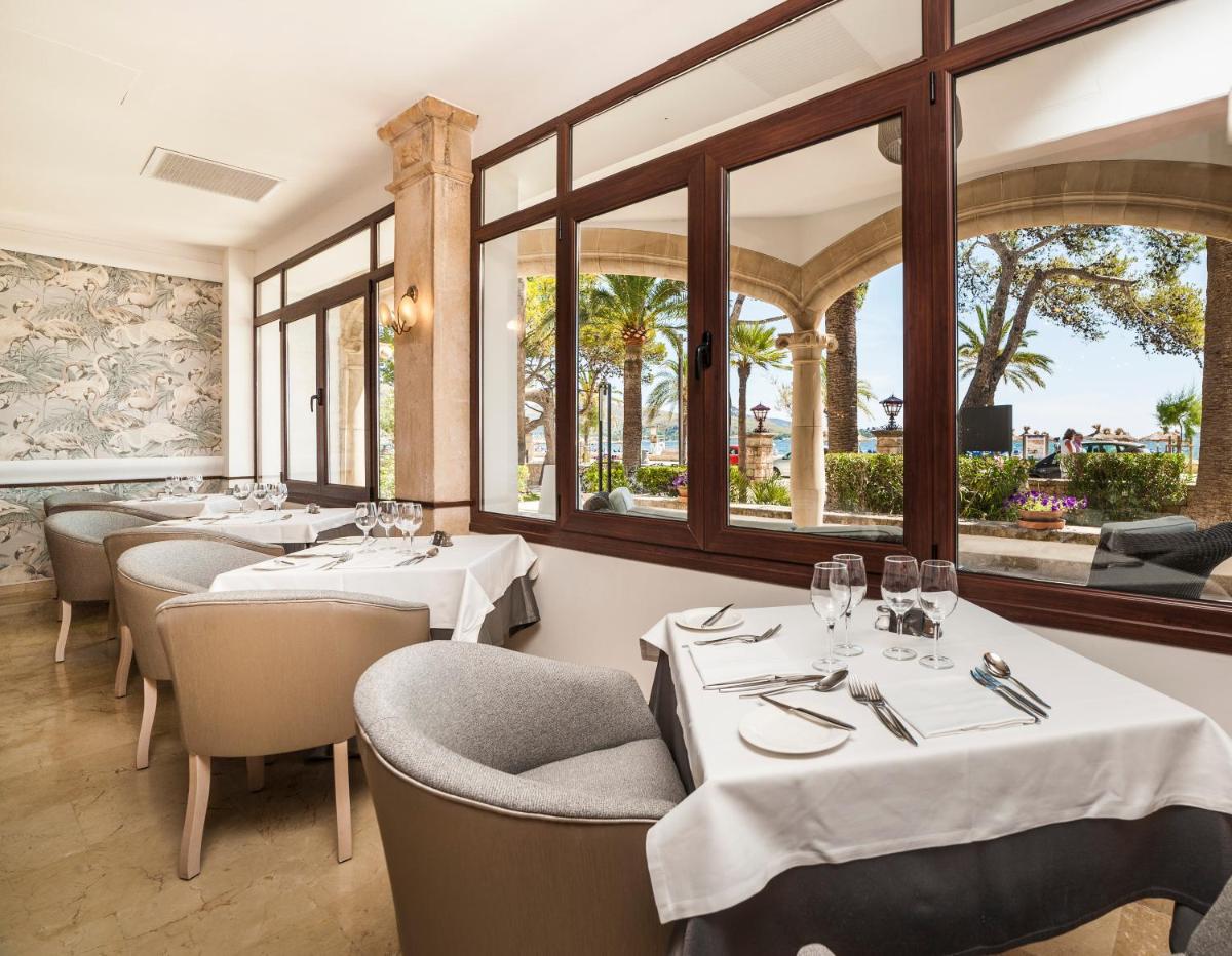 Un restaurante con mesas y sillas blancas y ventanas. en Hoposa Uyal, en Puerto Pollensa