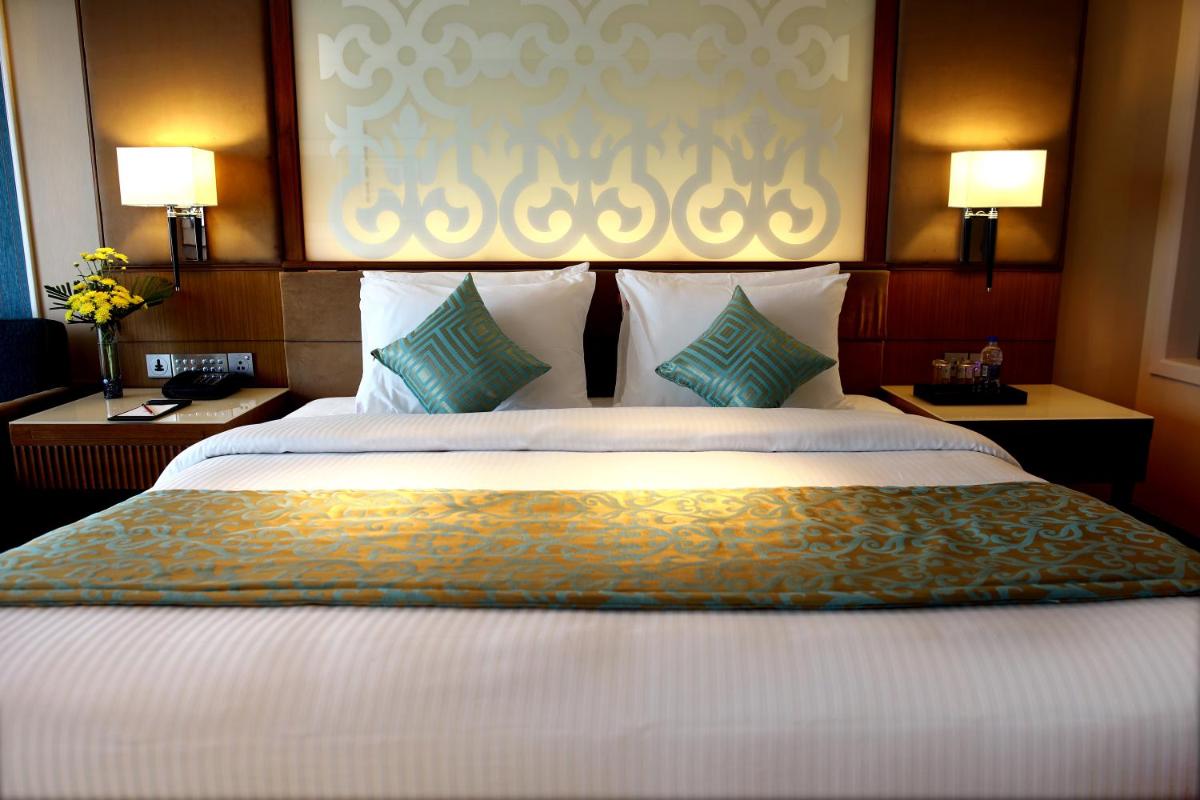 a large bed in a hotel room with two lamps at Ramada Plaza Chennai in Chennai