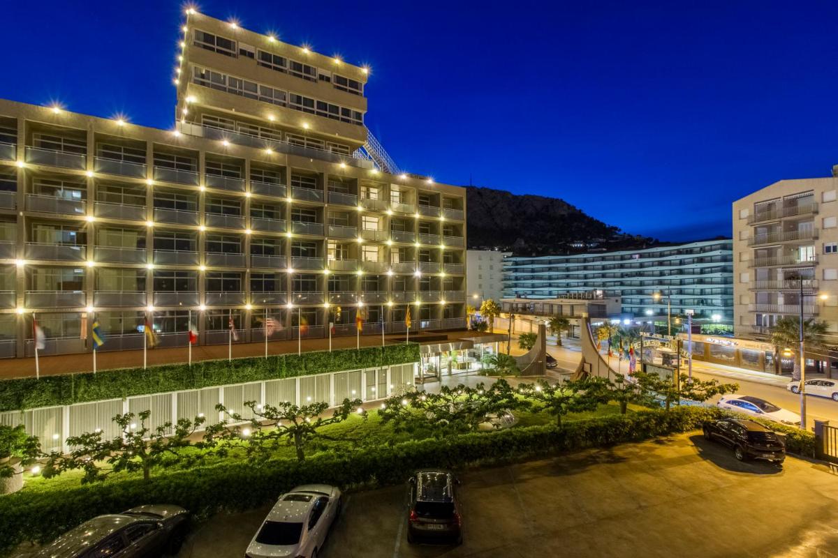 Un edificio con coches aparcados en un estacionamiento por la noche. en Hotel Panorama, en L'Estartit