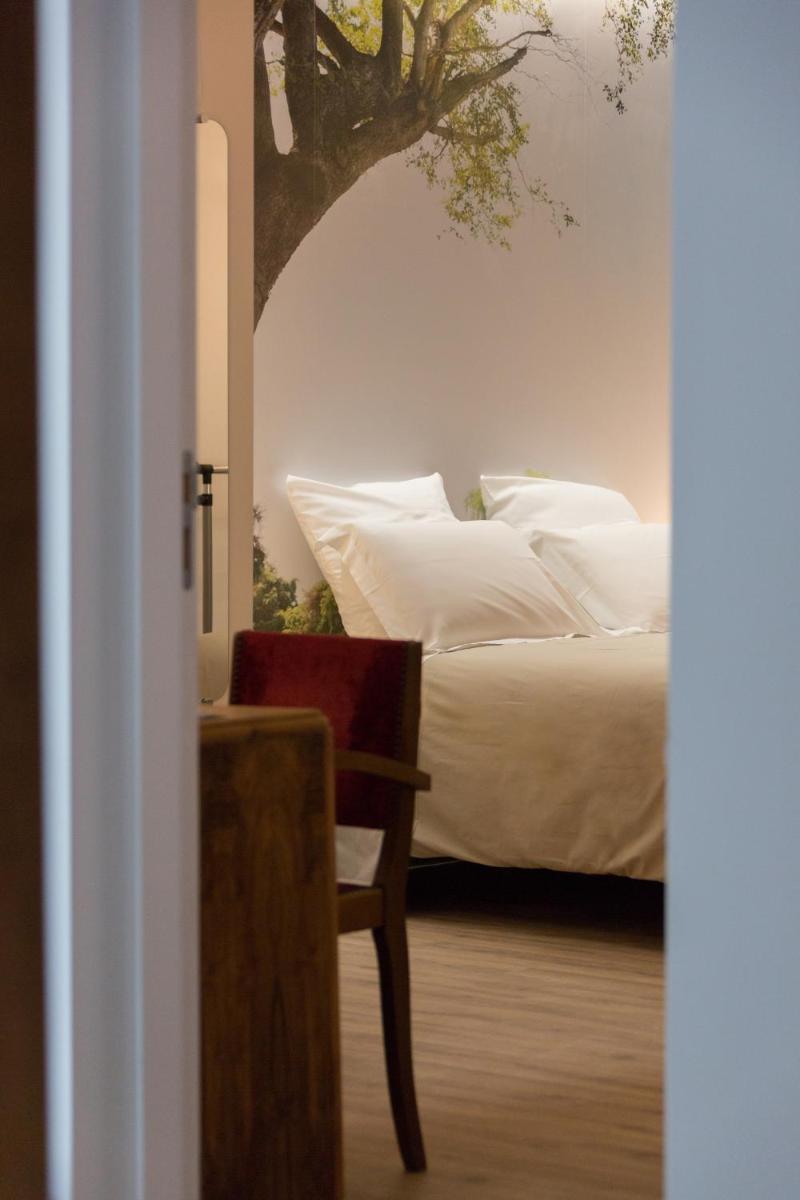 une chambre avec un lit aux oreillers blancs et une chaise dans l'établissement Le Miel des Muses, à Brive-la-Gaillarde