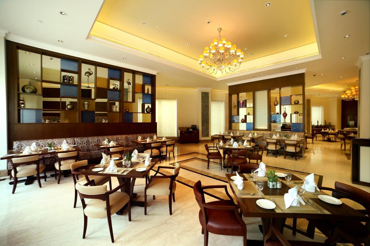 a restaurant with wooden tables and chairs and a chandelier at Ramada Plaza Chennai in Chennai
