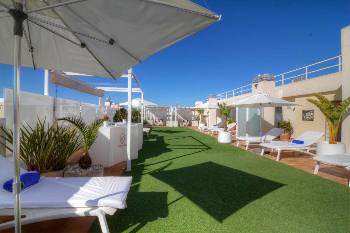 Un patio en la azotea con sillas blancas y una sombrilla. en Hotel Royal Plaza, en Ibiza