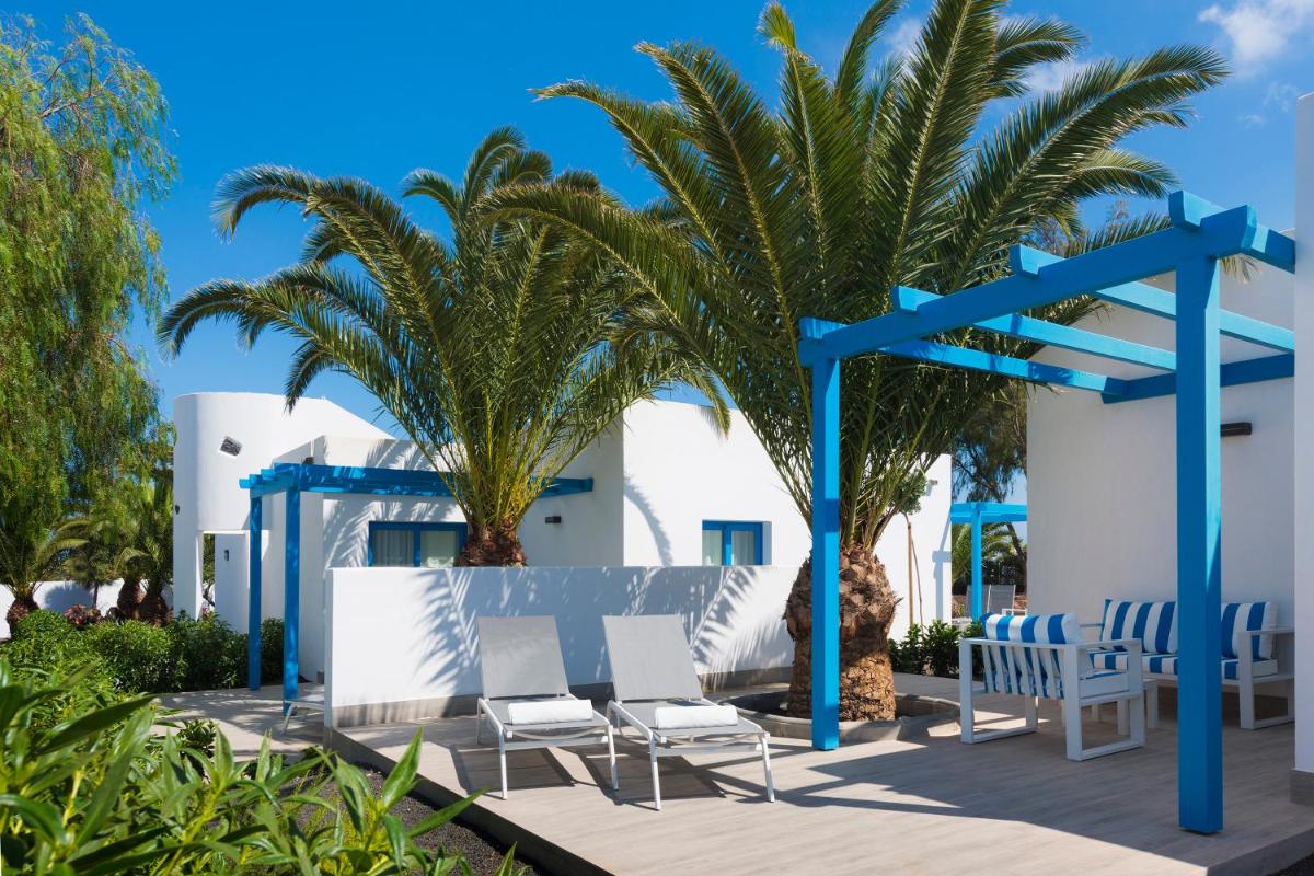un grupo de sillas y palmeras frente a un edificio en Elba Lanzarote Royal Village Resort, en Playa Blanca