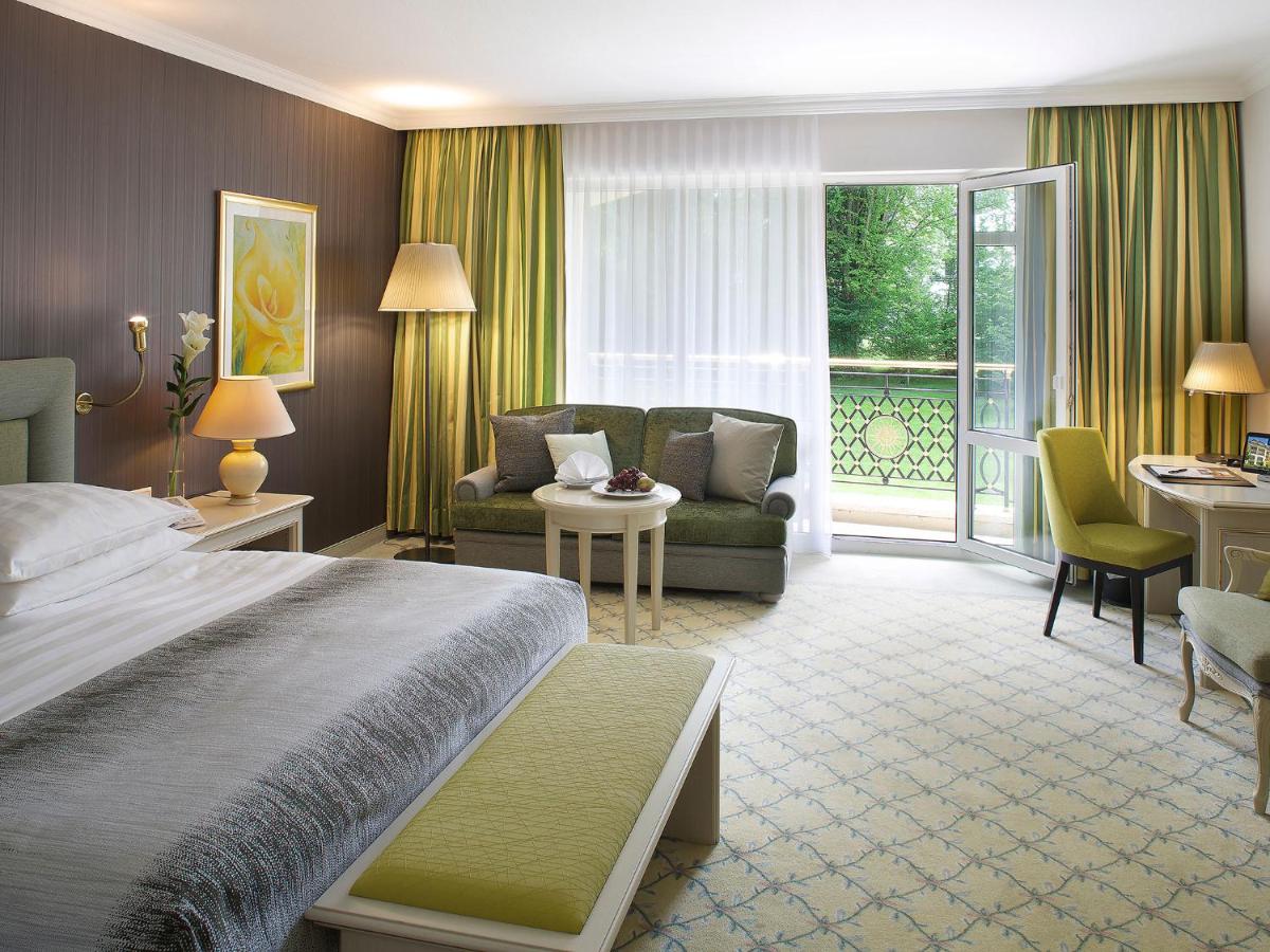ein Hotelzimmer mit einem Bett und einem Wohnzimmer in der Unterkunft Steigenberger Hotel Der Sonnenhof in Bad Wörishofen