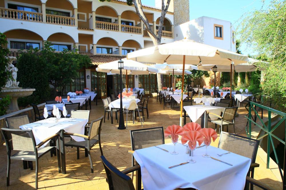 Un restaurante con mesas y sillas blancas y sombrillas. en Hotel Cala Gat, en Cala Ratjada