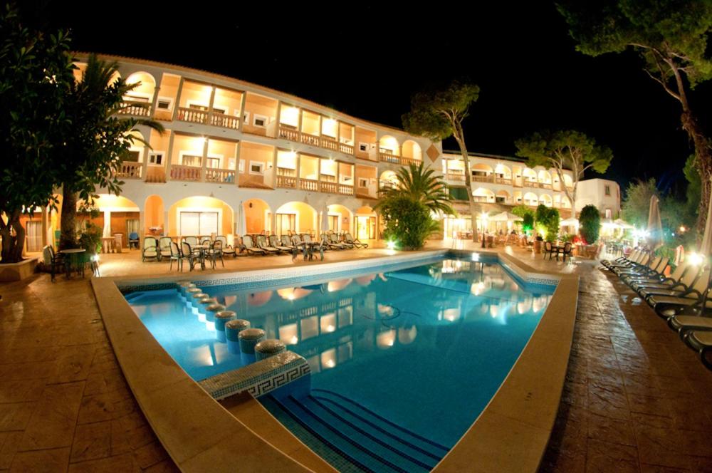 Una piscina frente a un hotel por la noche. en Hotel Cala Gat, en Cala Ratjada