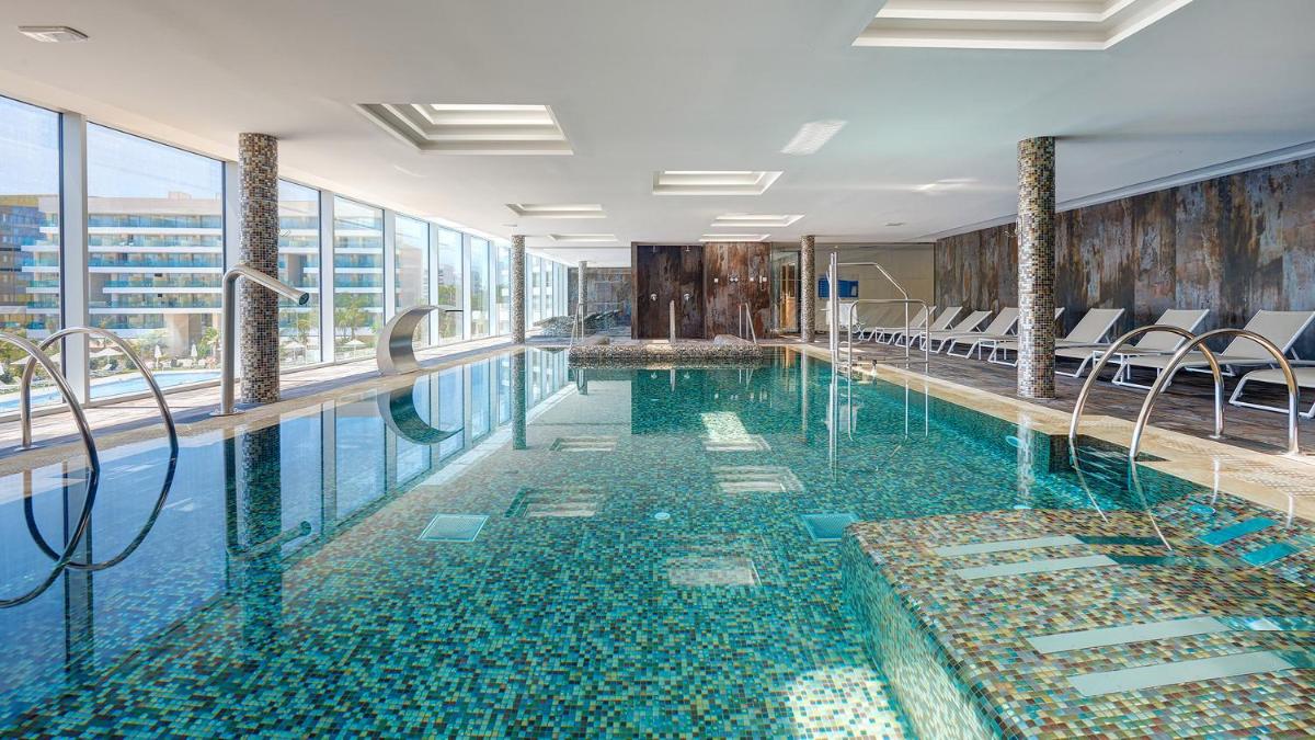 Una piscina en un hotel con sillas y ventanas. en Hipotels Playa de Palma Palace&Spa, en Playa de Palma