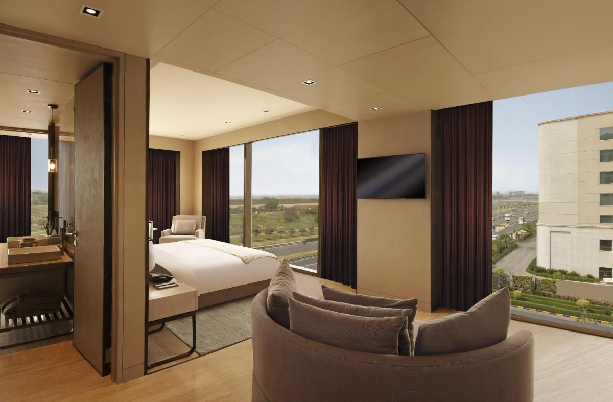 a hotel room with a bed and a bedroom with a view at Roseate House New Delhi in New Delhi a hotel room with a bed and a bedroom with a view at Roseate House New Delhi in New Delhi