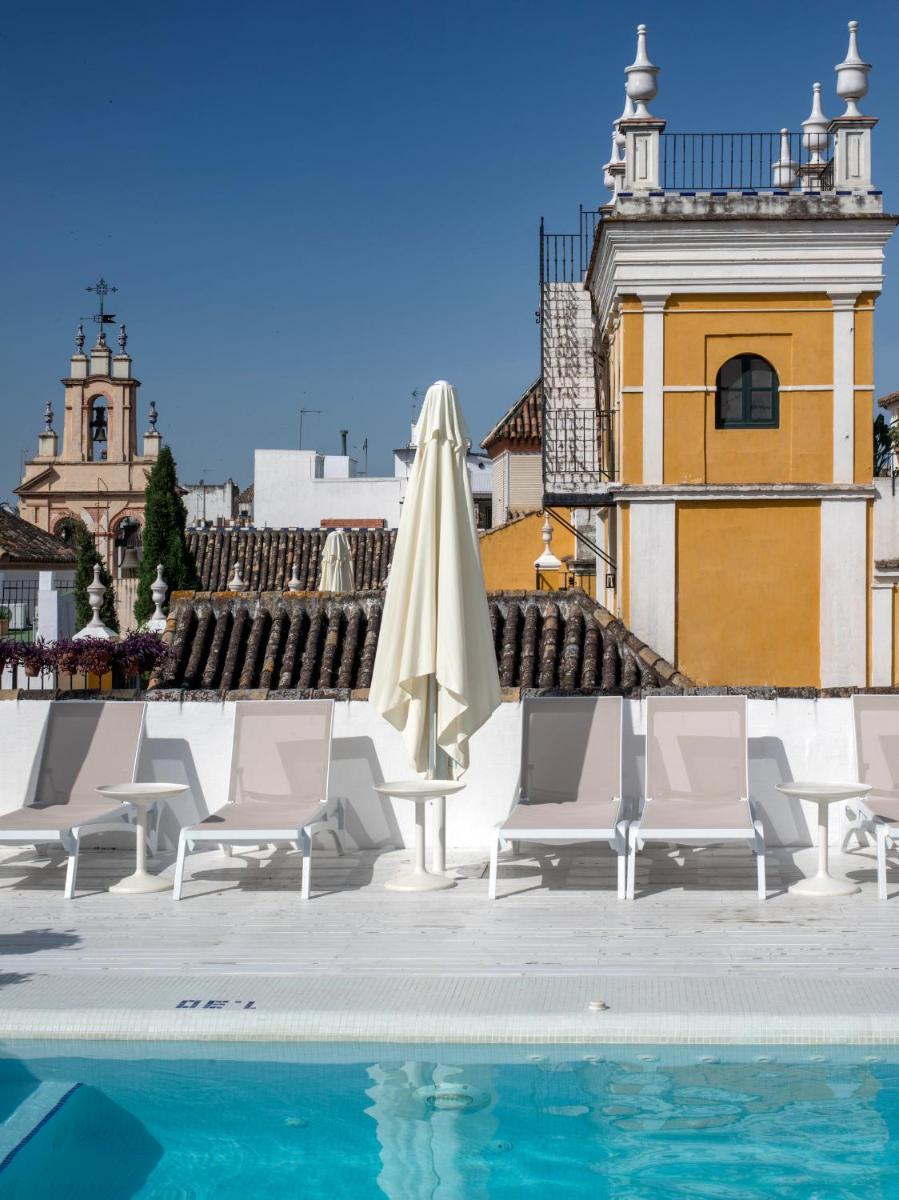 Una piscina con sillas y una sombrilla al lado de un edificio. en Hotel Las Casas de la Judería, en Sevilla
