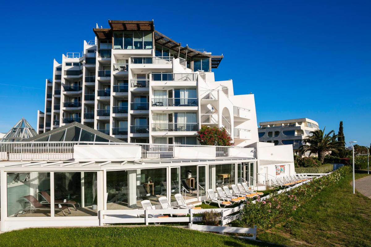 - un grand bâtiment blanc avec des chaises devant dans l'établissement Thalazur Port-Camargue - Hotel & Spa, au Grau-du-Roi