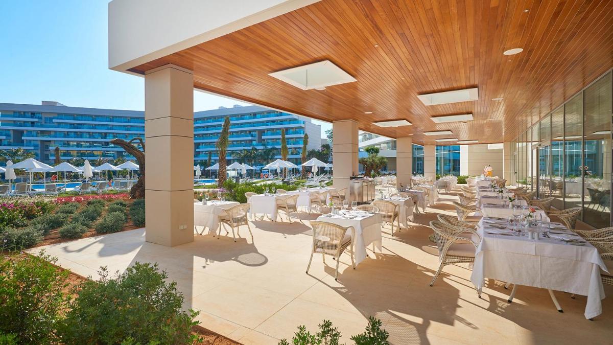 Un restaurante con mesas y sillas blancas y un edificio. en Hipotels Playa de Palma Palace&Spa, en Playa de Palma