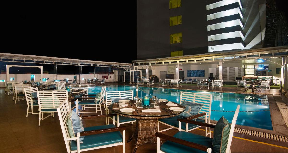 a swimming pool with tables and chairs next to a building at Sayaji Pune in Pune