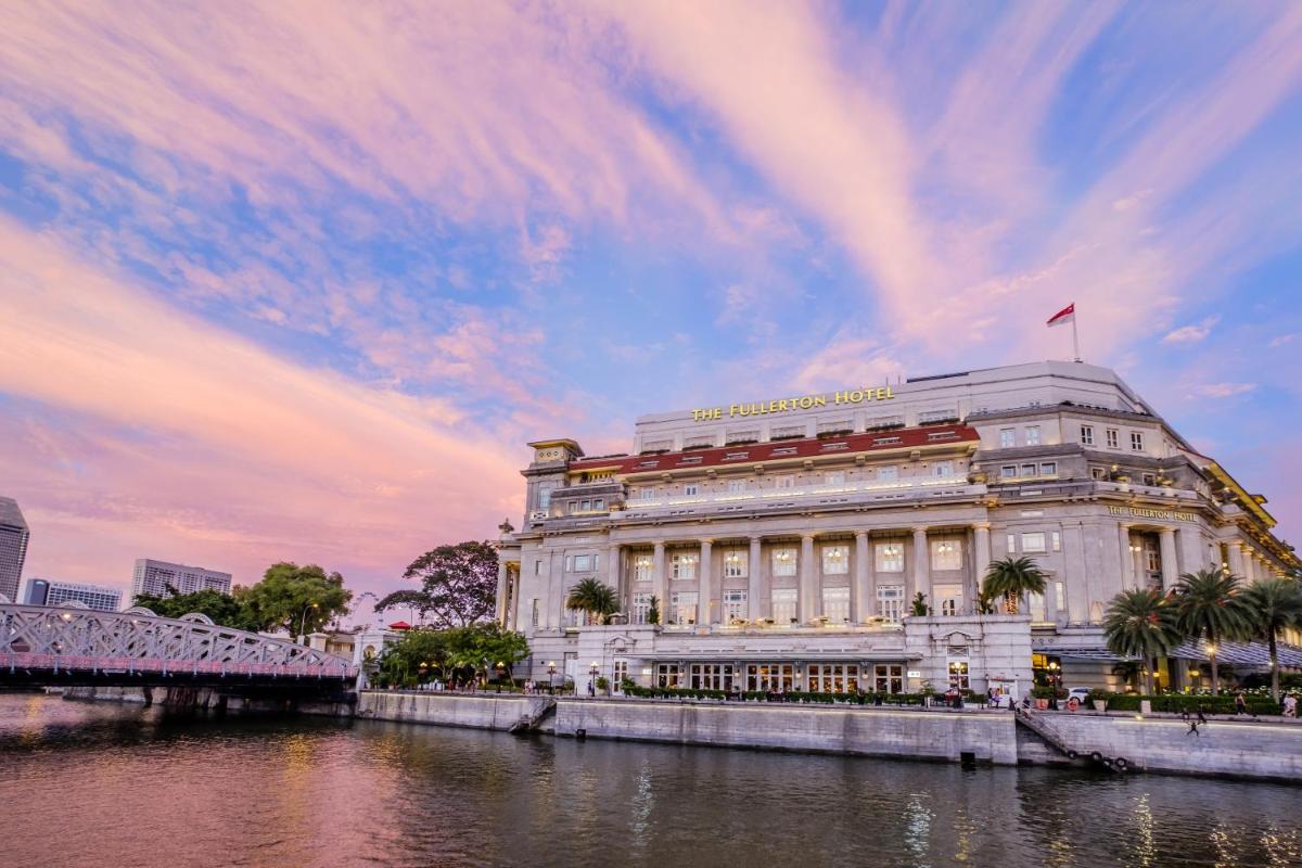 a building with a flag on top of it next to a river at The Fullerton Hotel Singapore in Singapore a building with a flag on top of it next to a river at The Fullerton Hotel Singapore in Singapore