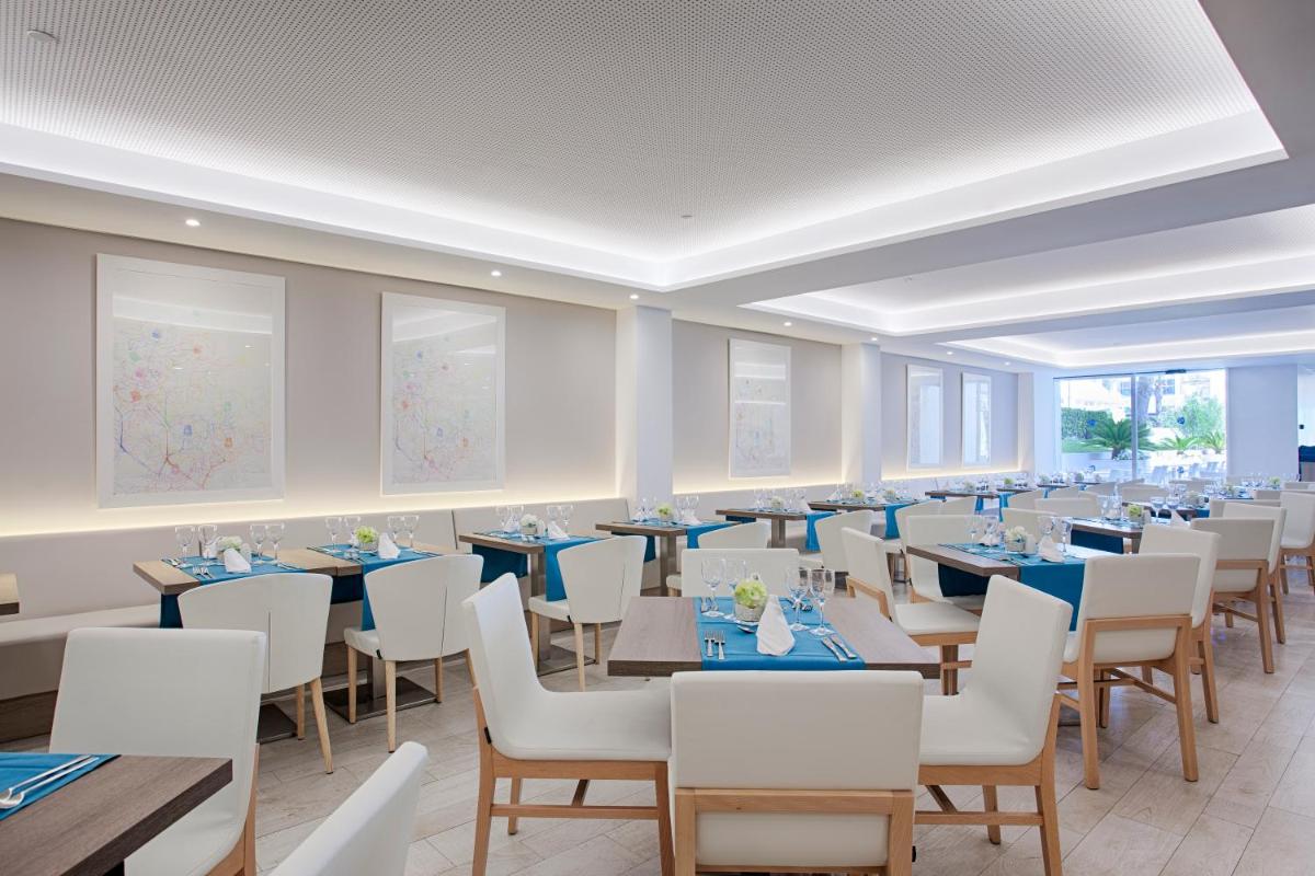 un gran comedor con mesas y sillas blancas en Grupotel Farrutx, en Can Picafort