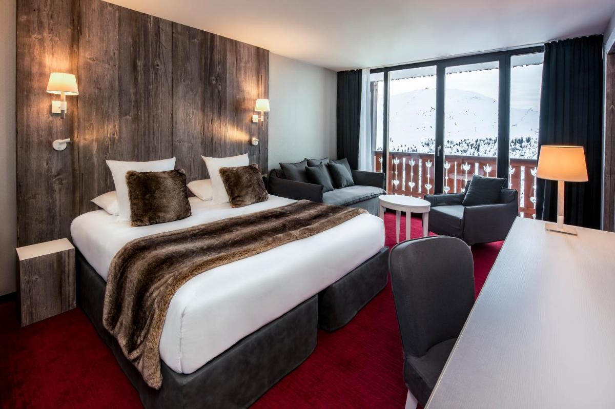 une chambre d'hôtel avec un grand lit et des chaises dans l'établissement Le Pic Blanc, à L'Alpe-d'Huez