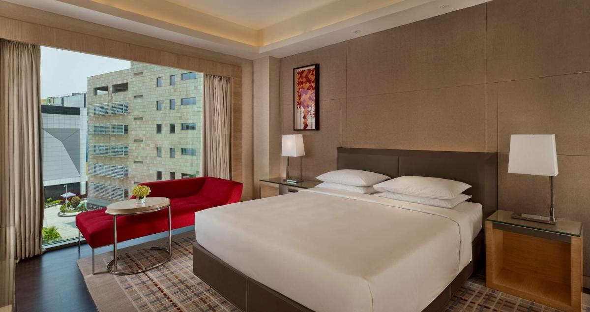 a bedroom with a large white bed and a red chair at Hyatt Regency Chandigarh in Chandīgarh