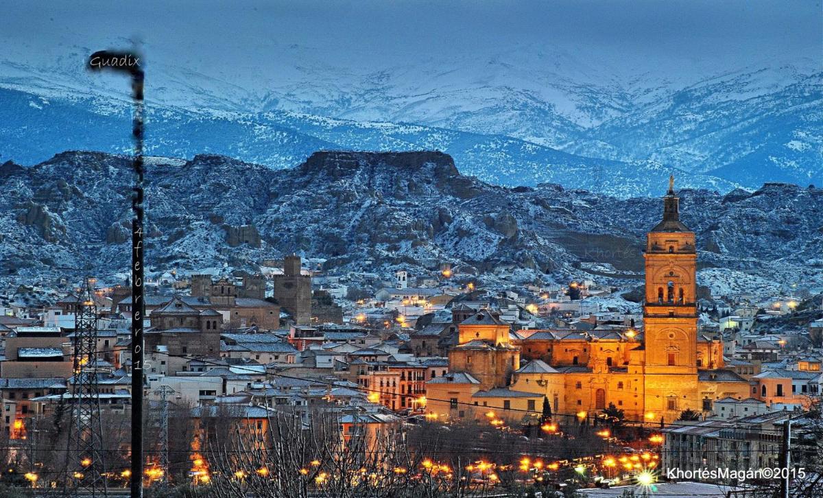 Una ciudad con una torre de reloj y un pueblo con montañas cubiertas de nieve. en Hotel Palacio de Oñate, en Guadix