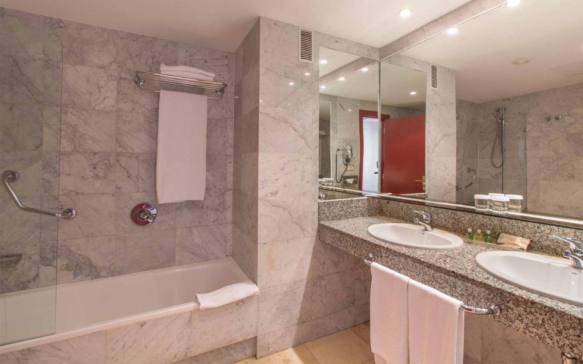 Un baño con dos lavabos, una bañera y una ducha. en Hotel Cleopatra Palace, en Playa de las Américas