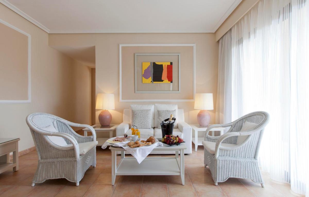 una sala de estar con sillas blancas y una mesa con comida. en Lago Garden Apart-Suites & Spa Hotel, en Cala Ratjada