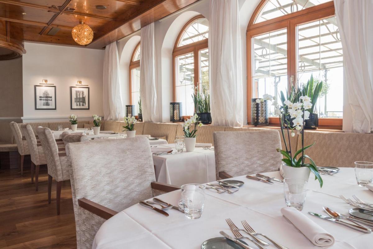 ein Restaurant mit weißen Tischen und Stühlen und Fenstern in der Unterkunft Der Birkenhof Spa & Genuss Resort in Hofenstetten ein Restaurant mit weißen Tischen und Stühlen und Fenstern in der Unterkunft Der Birkenhof Spa & Genuss Resort in Hofenstetten
