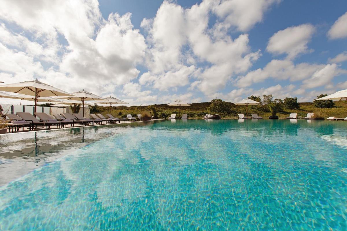 ein großes Schwimmbecken mit Liegestühlen und Sonnenschirmen in der Unterkunft A-ROSA Sylt in List