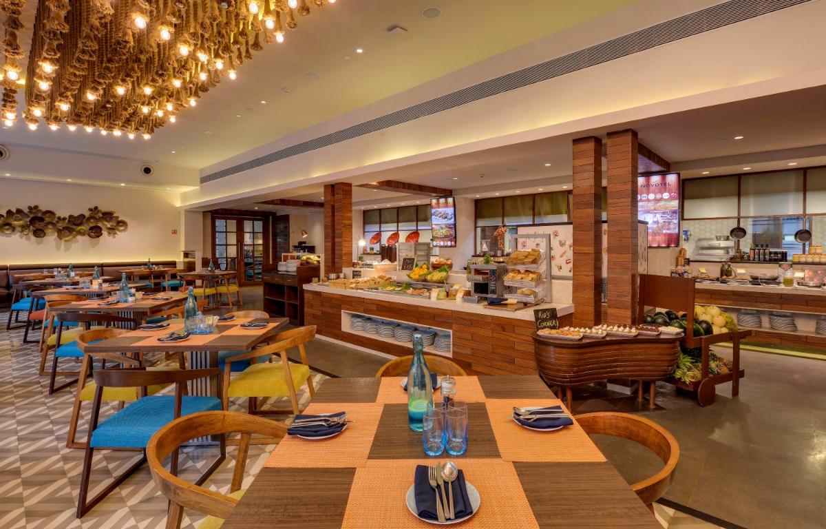 a restaurant with wooden tables and chairs and a counter at Novotel Goa Candolim in Candolim a restaurant with wooden tables and chairs and a counter at Novotel Goa Candolim in Candolim