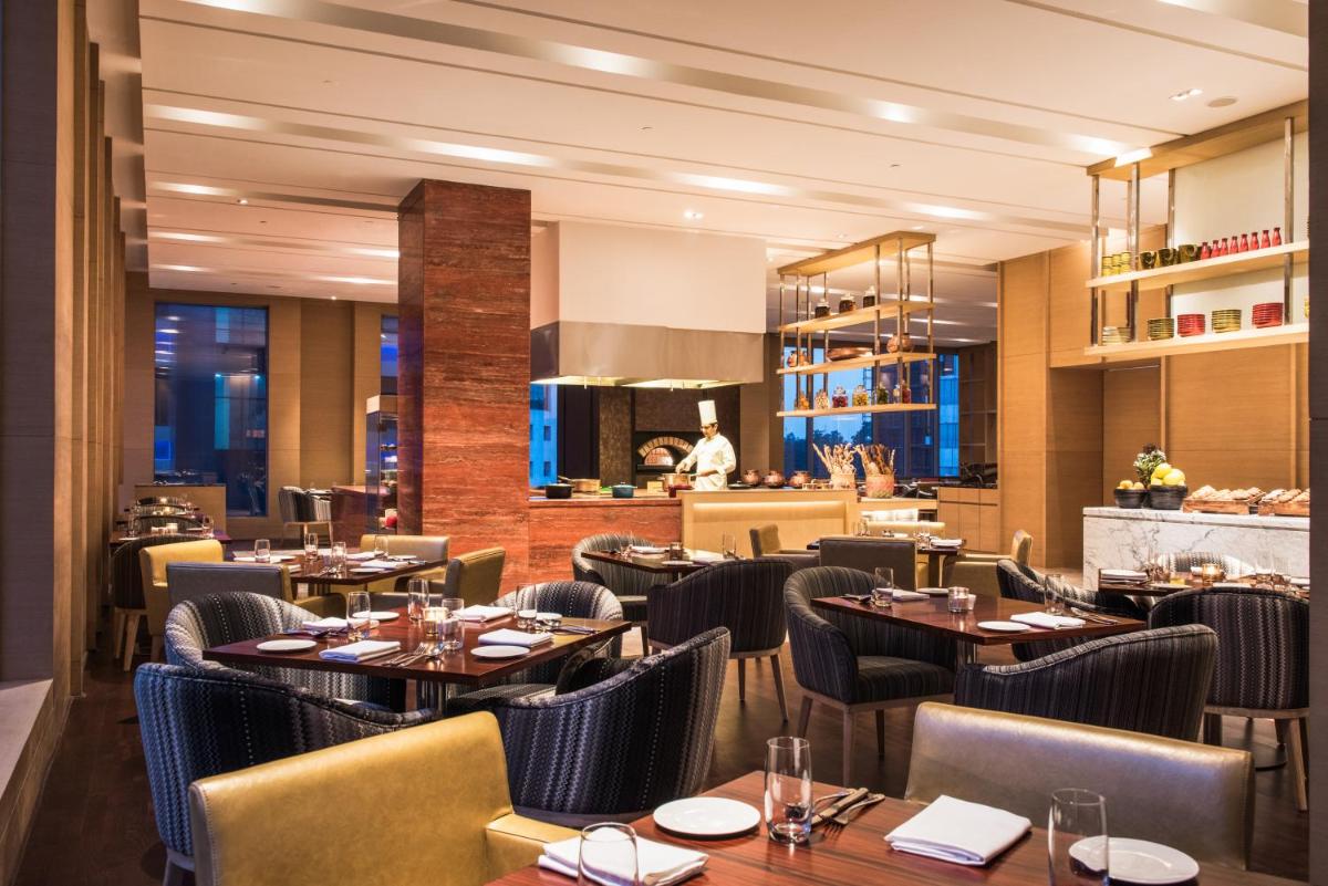 a restaurant with tables and chairs and a chef in the kitchen at Hyatt Regency Lucknow Gomti Nagar in Lucknow