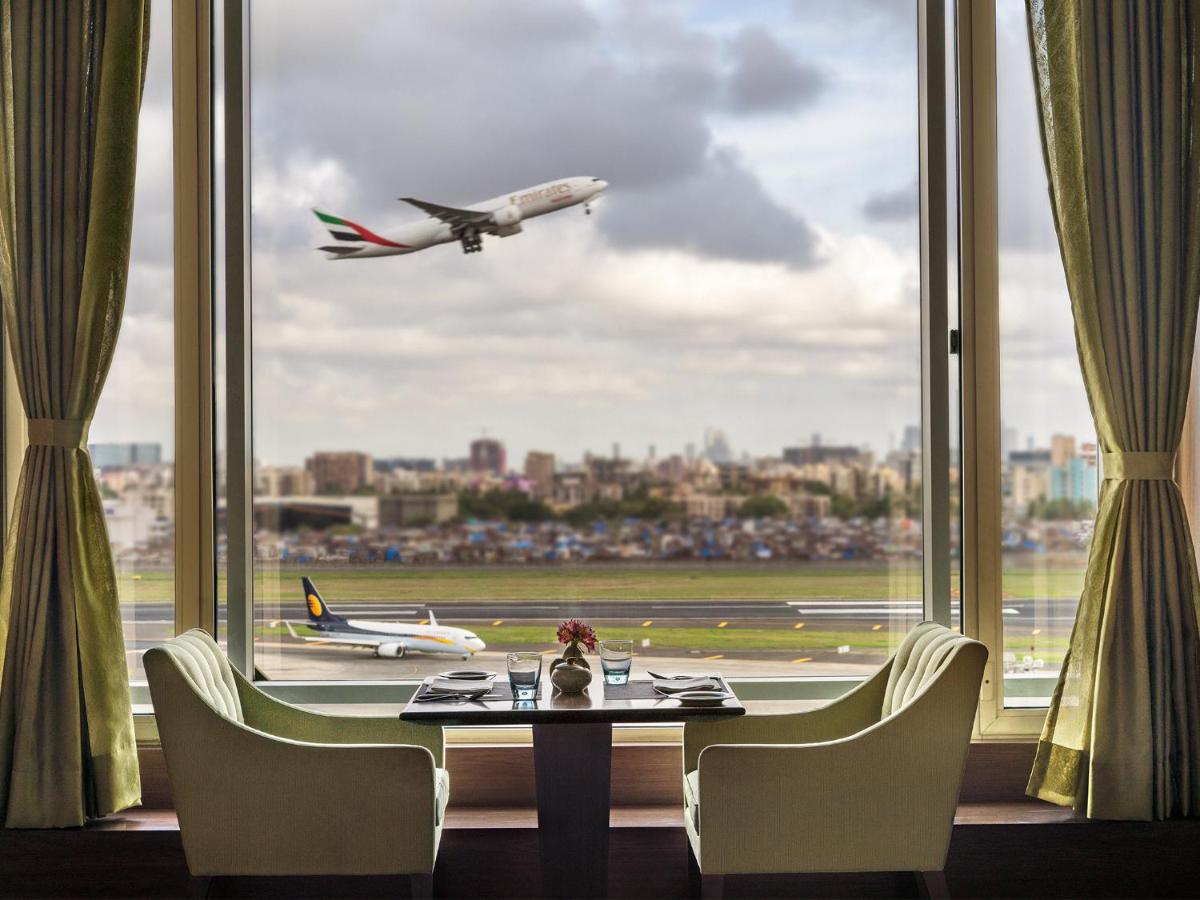 a table and chairs in front of a window with an airplane at Taj Santacruz in Mumbai