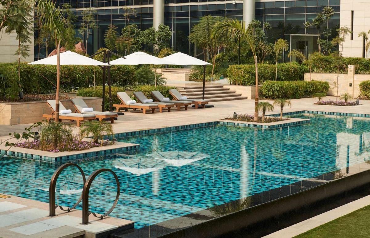 a swimming pool with chairs and umbrellas in a building at Andaz Delhi, by Hyatt in New Delhi a swimming pool with chairs and umbrellas in a building at Andaz Delhi, by Hyatt in New Delhi