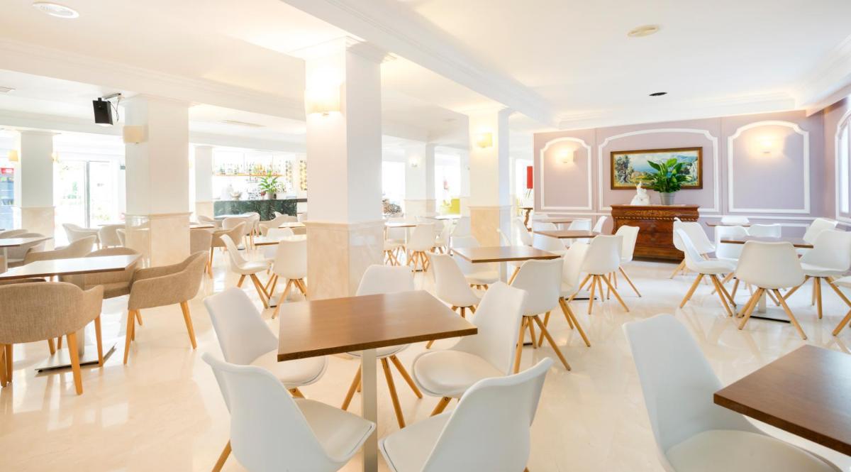 Un comedor con mesas y sillas blancas. en Hotel Morito, en Cala Millor